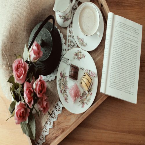 A wooden tray holding a book, a cup of tea, and fresh flowers.