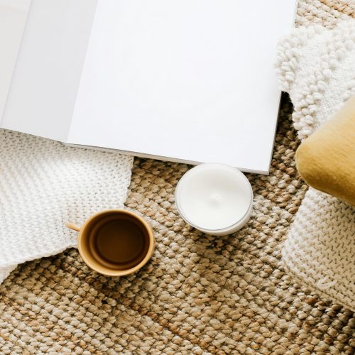 A cozy setup with a journal, coffee cup, and pillow on a rug.