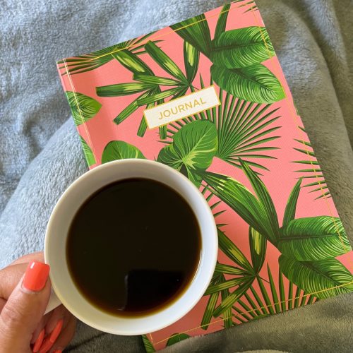 A vibrant tropical notebook sits next to a cup of coffee.