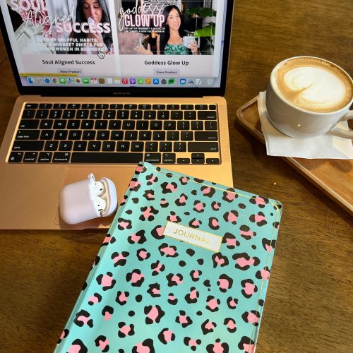 A notebook, coffee, and laptop on a wooden table.