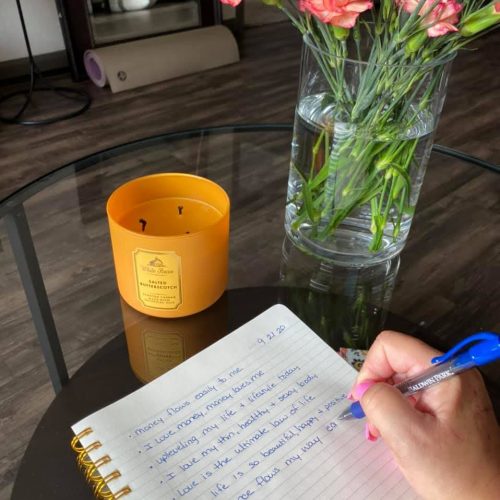 a person writing on a notepad next to a vase of flowers