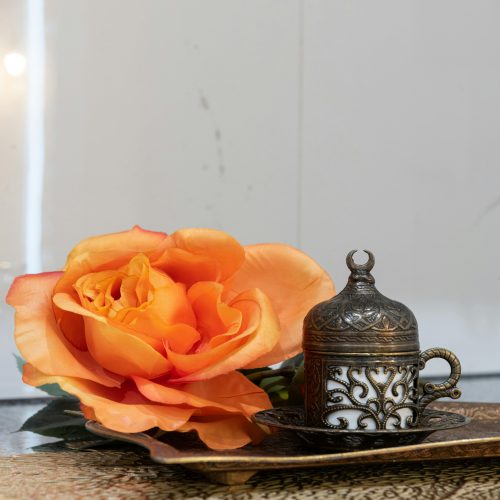 an orange rose sitting on top of a table next to a tea pot