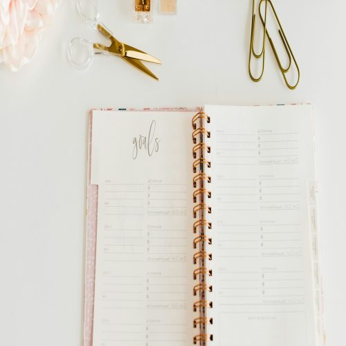 a planner, pen, scissors, and other office supplies on a desk