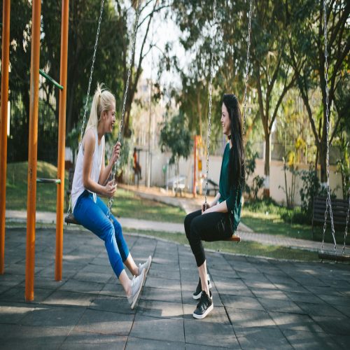 two women sitting on swings in a park