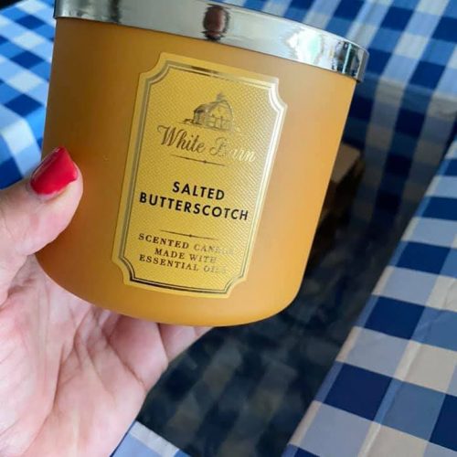 A hand holding a candle in a box on a checkered tablecloth.