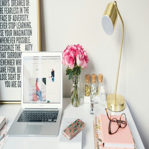 a white desk with a laptop and pink flowers