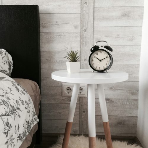 White table with clock next to bed in cozy bedroom setting.