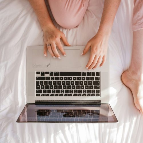 a woman laying in bed with her hands on a laptop