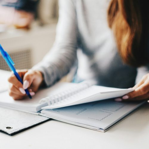 A woman sitting at a desk, writing in a notebook with a pen.