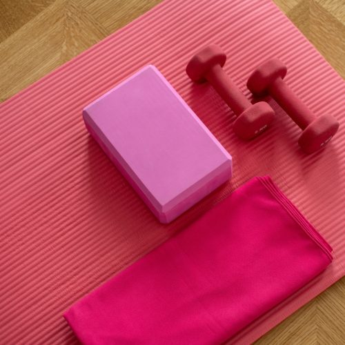 Pink yoga mat, towel, and dumbbells on wooden floor for a workout session.